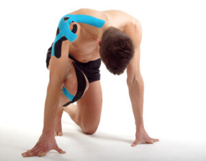 Athlete taking starting position on white background, Shoulder and knee taped with kinesiology tape. Front viewpoint